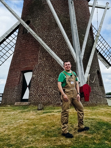 Der Müller Leon Joachims steht in brauner Arbeitskleidung vor seiner historischen Windmühle.