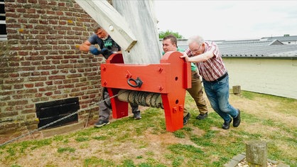 Drei Männer bewegen die Mühlenflügel mit einer Winde in Position.
