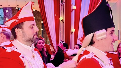 Markus Gurok auf einer Sitzung der roten Funken. Er ist selbst verkleidet und arbeitet an der Perücke eines Mannes.