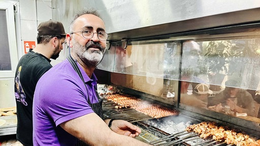 Gründer Erol Günes steht an einem Holzkohlegrill. Er trägt eine Schürze.