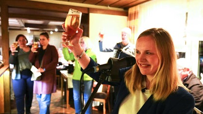 Pfarrerin Eva Meisel steht in einer Kneipe in Bönen und hebt ein Bierglas in die Luft, rundherum stehen weitere Gäste mit Biergläsern
