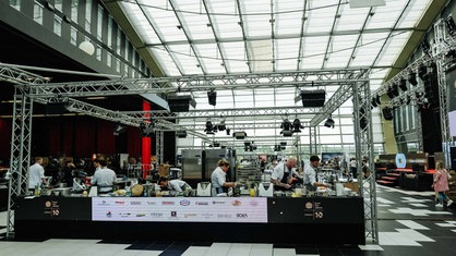 Ein große Halle. In der Mitte befindet sich ein abgegrenzter Bereich. Dort kochen die Köche.
