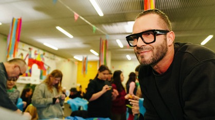 Sven West von "Die Räuber" im Portrait. Im Hintergrund basteln Kinder an Karnevalskostümen.