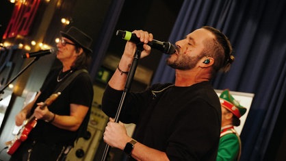 Sven West Frontmann der "Räuber" auf der Bühne mit Mikrofon. Links von ihm der Bassist.