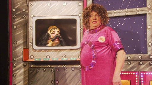 Alexander Moll steht in pinker Kleidung und mit Perücke auf der Bühne im Theater Filmdose in Köln