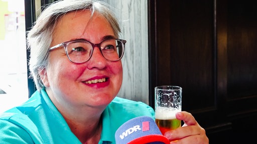 Eine Frau sitzt mit einem Glas Kölsch am Tisch eines Brauhauses in Köln.
