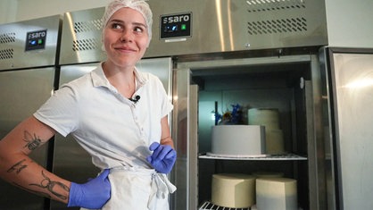 Lilian Weschke steht vor einem Kühlschrank, der mit Torten gefüllt ist. Sie trägt blaue Handschuhe und eine Haube.