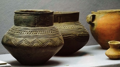 Drei Urnen und eine kleine Vase. Zwei Vasen sind grau und haben Muster auf der Oberfläche.