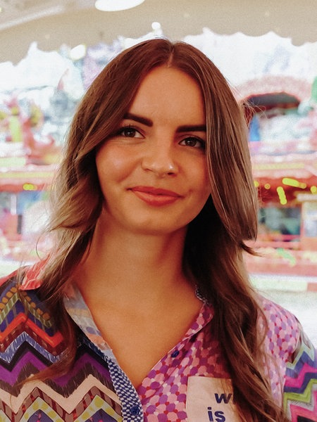 Lisa Lemoine steht in der Bude ihrer Familie, im Hintergrund ein buntes Kirmes-Fahrgeschäft