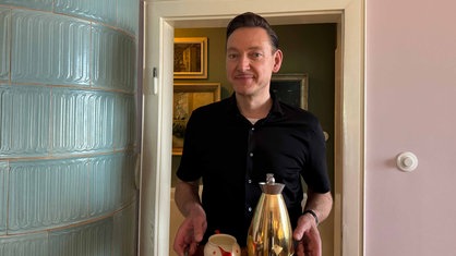Remco Schaumann steht in seiner Villa aus den 50er-Jahren neben einem alten Kachelofen, in der Hand hält er ein Tablett mit Kaffeekanne