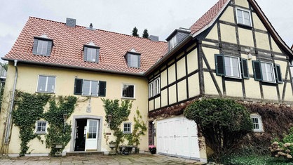 Die Villa aus den 50er-Jahren von außen, es ist ein großes Haus mit hellgelber Fassade und Fachwerk