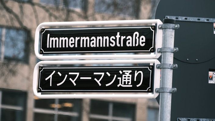 Ein Straßenschild mit der Aufschrift "Immermannstraße". Darunter das Wort auf Japanisch.