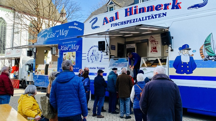 Auf dem Marktplatz stehen drei Verkaufswagen nebeneinander, davor einige Kunden.