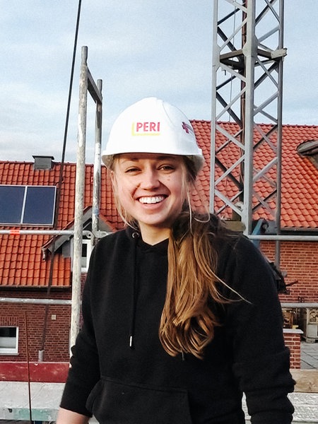 Eine junge Maurermeisterin steht mit Helm auf einer Baustelle.
