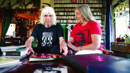 Ein Mann und eine Frau sitzen auf dem Sofa und blicken auf ihre Musiksammlung auf dem Tisch.