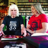 Ein Mann und eine Frau sitzen auf dem Sofa und blicken auf ihre Musiksammlung auf dem Tisch.