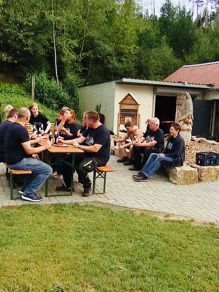 Mehrere Menschen sitzen auf Bänken und Steinen und essen gemeinsam.
