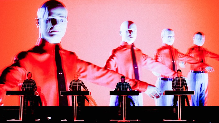 Die vier Musiker der klassischen Kraftwerk-Besetzung während eines Konzerts. Im Hintergrund sind die Bandmitglieder als riesige Puppen auf einer Videowand abgebildet.