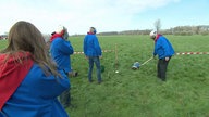 Einwohner von Herzebrock-Clarholz stehen mit Ohrenschützern auf einem freien Feld, einer hält eine brennende Fackel an den Boden einer Milchkanne.