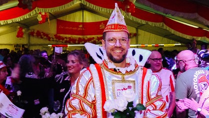 Henning Bargmann steht in seinem Prinzen-Ornat im Festzelt und grinst.