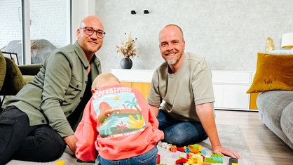 Dennis und Danny lächeln in ihrem Zuhause.