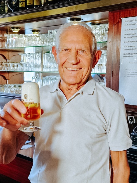 Toni Pinna, ein 86-jähriger Mann, hält ein Bier in der Hand und grinst.