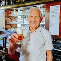 Toni Pinna, ein 86-jähriger Mann, hält ein Bier in der Hand und grinst.
