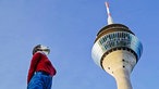 Eine Säulenheiligen-Skulptur in Düsseldorf zeigt eine Frau, die zum Himmel hinaufblickt. Dahinter befindet sich der Rheinturm.