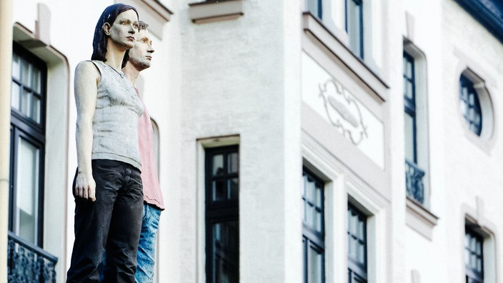 Die Skulptur eines Paares steht auf einer Litfaßsäule.
