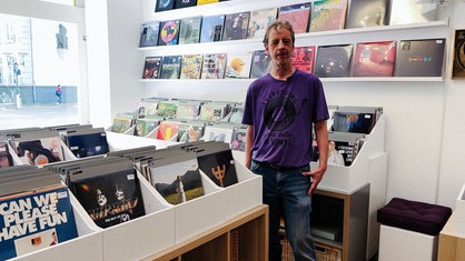 Julian von Heyl steht in seinem Plattenladen und trägt ein violettes T-Shirt.