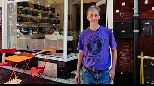 Julian von Heyl mit violeten Shirts steht vor seinem Plattenladen