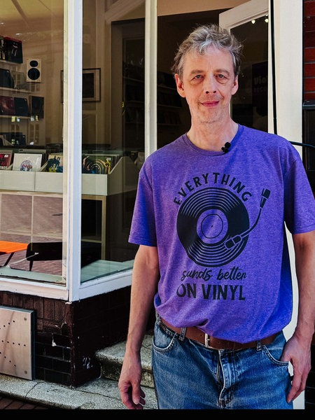 Julian von Heyl mit violeten Shirts steht vor seinem Plattenladen