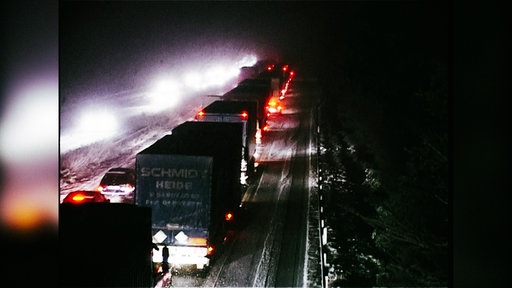 Auto und Lkws stehen auf einer Autobahn im Schnee im Stau.