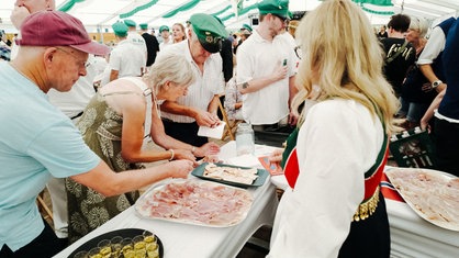 Menschen drängen sich um den Norwegerstand auf dem Schützenfestzelt und bedienen sich an dem Essen. Hinter den Tischen steht Ana Radermacher.