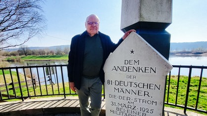 Ein Mann neben einem Denkmal, im Hintergrund ein Fluss 