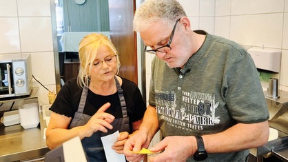 Eine Frau und ein Mann schauen auf einen gelben Zettel, den der Mann in seinen Händen hält.