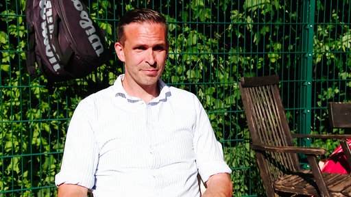 Timo Höppner sitzt bei Sonnenschein am Rand eines Speckbrettspielfelds