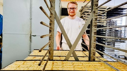 Ein junger Mann steht in einer Backstube vor einem Blech mit Spekulatius und lächelt in die Kamera.