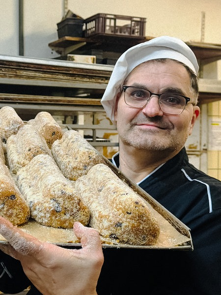 Bäckermeister Jörg Liese in einer Bäckerstube. Er hält ein Blech mit einigen Christstollen in die Kamera.