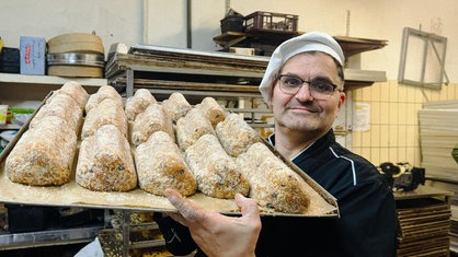 Bäckermeister Jörg Liese in einer Bäckerstube. Er hält ein Blech mit einigen Christstollen in die Kamera.