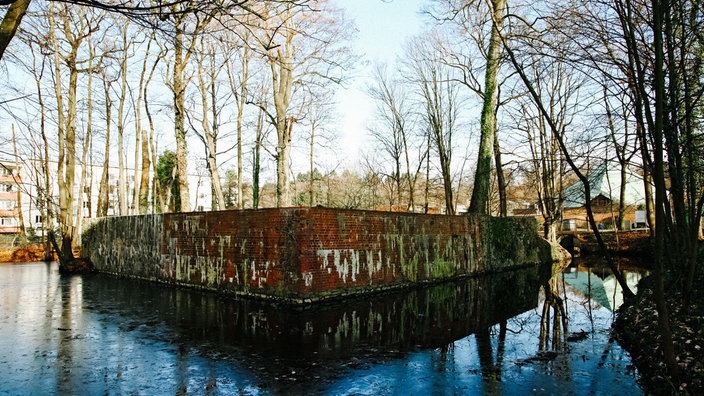 Eine Ruine, die halb verfallen im Wasser unter Bäumen steht