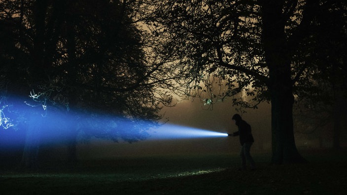 Ein Mann im dunklen Wald mit einer Taschenlampe.