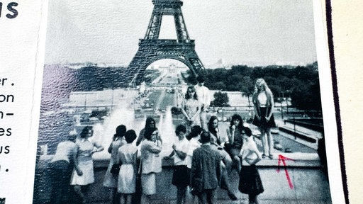 Eine Reisegruppe steht vor dem Eiffelturm. Einige schauen in die Kamera und einige schauen auf den Eiffelturm.