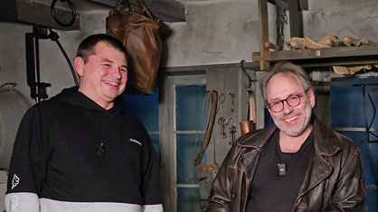 Elmar Zielke und Frank Jannusch stehen in einer nachgebauten historischen Schmiede und lachen