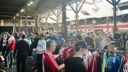 Eine große Halle, gefüllt mit Kleiderstangen voll Fußballtrikots und Menschen.