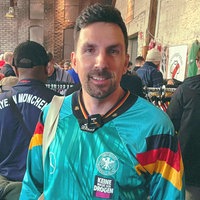 Christian Rottmeier, ein schwarzhaariger Mann mit Dreitagebart, steht im türkisen Trikot vor einer Kleiderstange in einer roten Backsteinhalle.