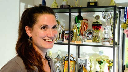 Maura Porrmann vor einem Regal, gefüllt mit dutzenden Pokalen