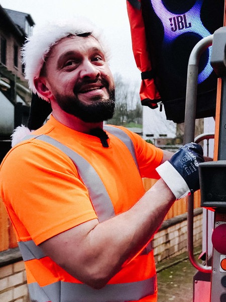 Alex Rubchev steht an einem Müllwagen. Auf dem Kopf trägt er eine Weihnachtsmann-Mütze. Er lächelt.