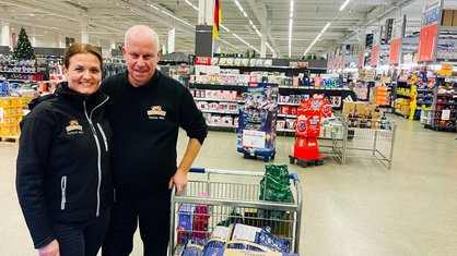 Eine Frau und ein Mann stehen neben einem Einkaufswagen im Großmarkt
