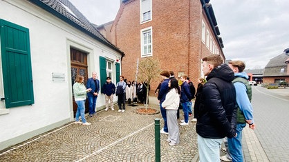 Eine Gruppe von Schülern und Schülerinnen hat sich vor einem Haus versammelt. 
